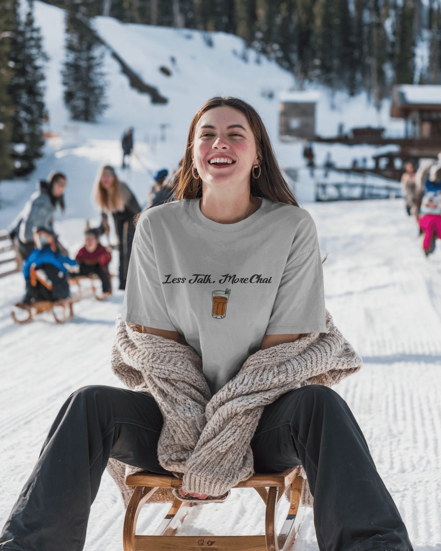 Person sitting on a sled in a snowy landscape with a 'Less Talk, More Chai' shirt.
