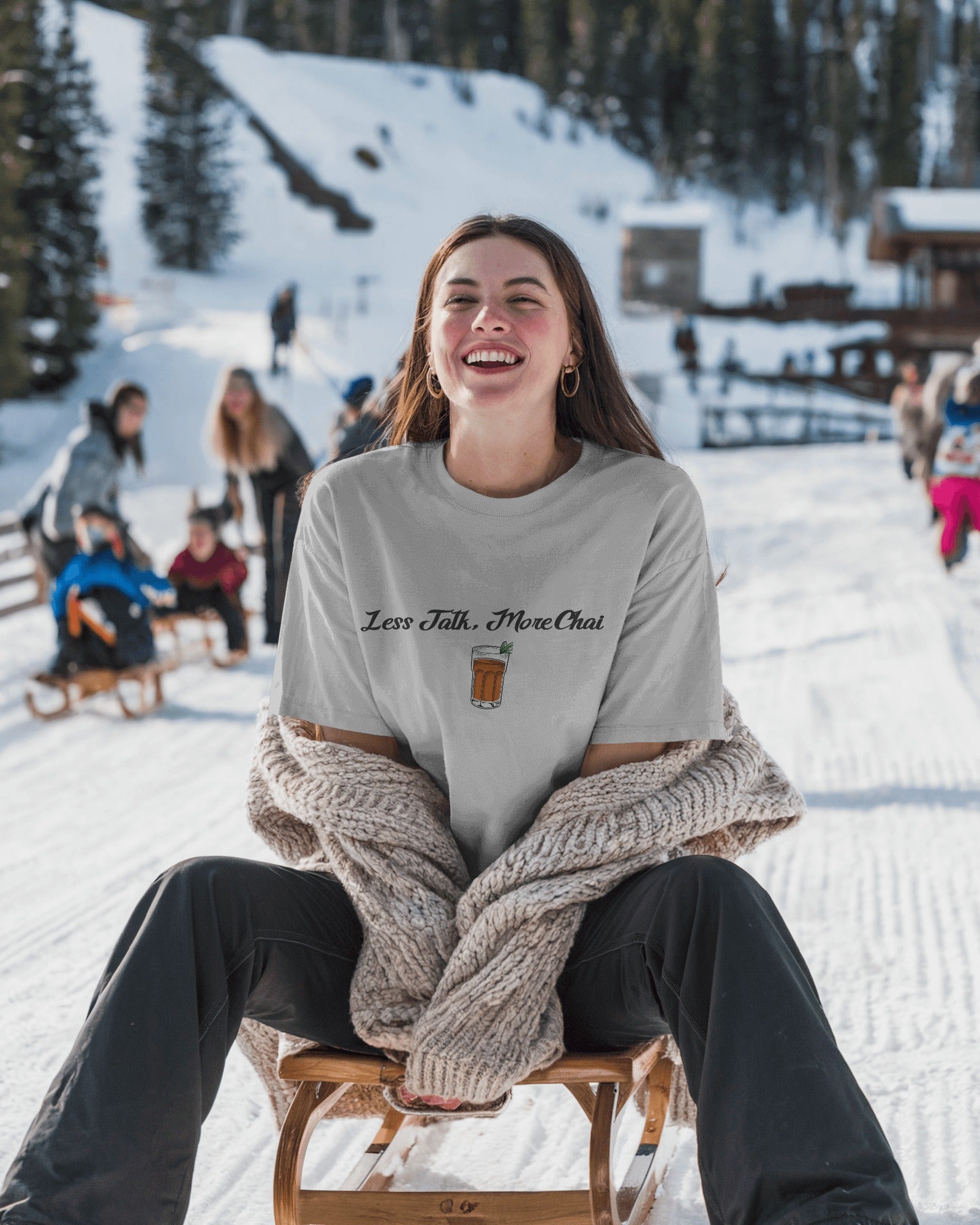Person sitting on a sled in a snowy landscape with a 'Less Talk, More Chai' shirt.